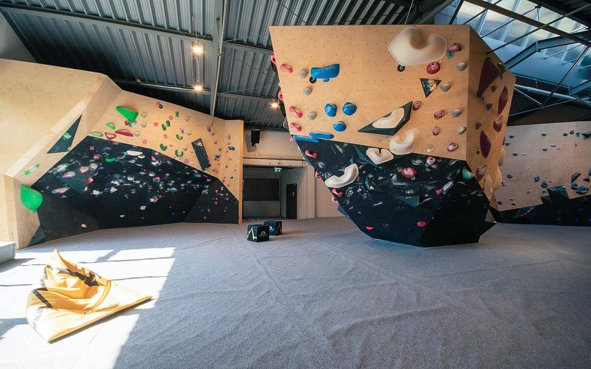 Boulderbereich im Stuntwerk Trostberg mit vielseitigen Kletterwänden, farbigen Griffen und großen Volumen. Helle Halle mit hohen Decken und großzügiger Mattenfläche für sicheres Bouldern auf allen Levels.
