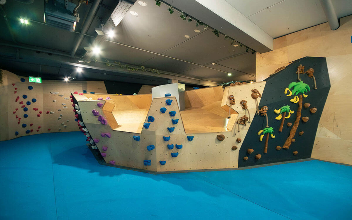 Kinderboulderbereich im Stuntwerk Trostberg mit kinderfreundlichen Klettergriffen in Tierformen und Seilelementen. Zwei Kinder klettern spielerisch an der Boulderwand; sichere Holzstrukturen und farbenfrohes Design fördern Spaß, Motorik und Bewegungsfreude.